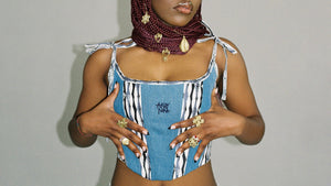 closeup of a black wmaon wearing a vintage styled corsed handmade of recycled blue denim jeans and African pattern print fabric. unique Afro-European streetwear