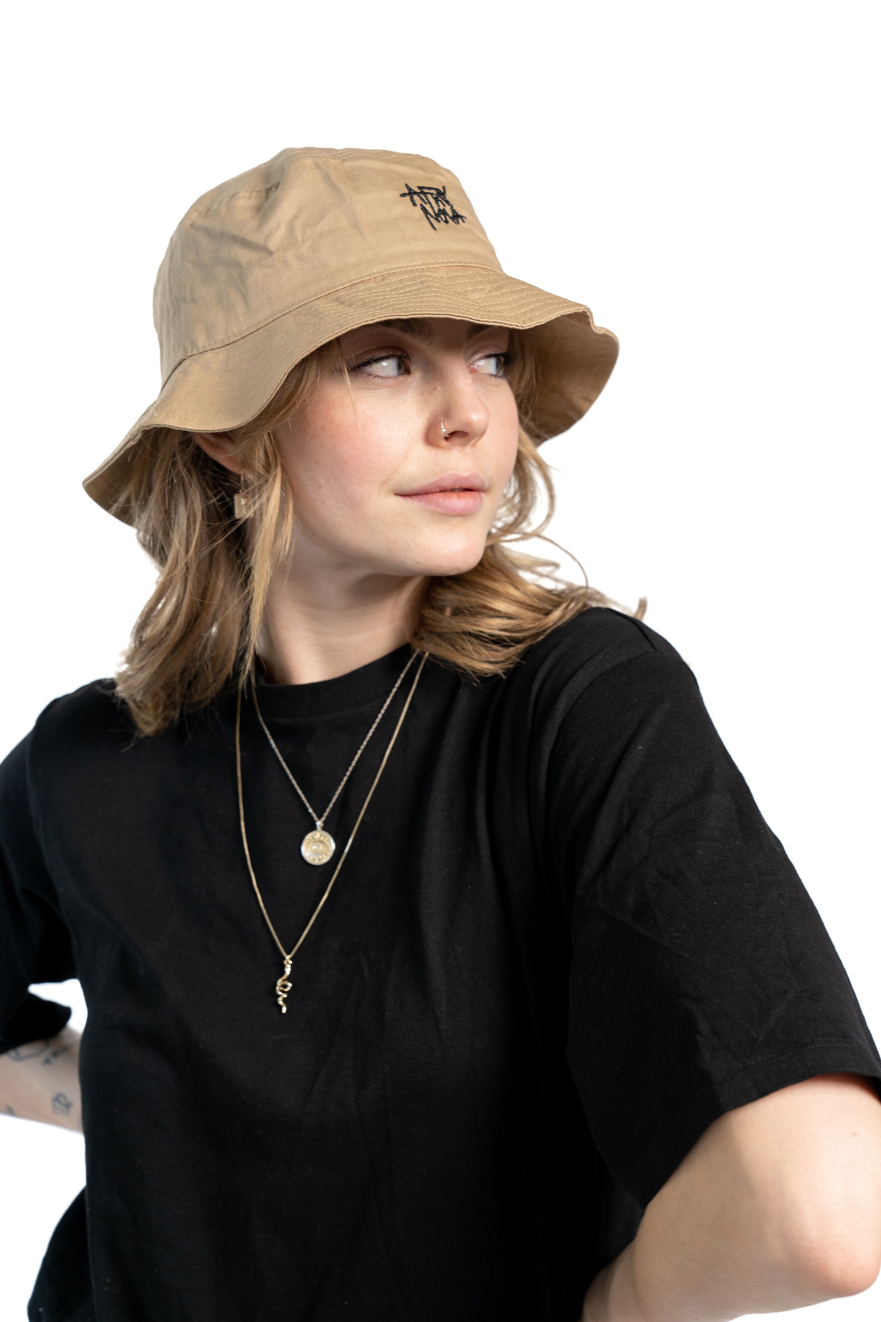 Frau mit blonden Haaren und schwarzem T-Shirt trägt einen beigen Fischerhut