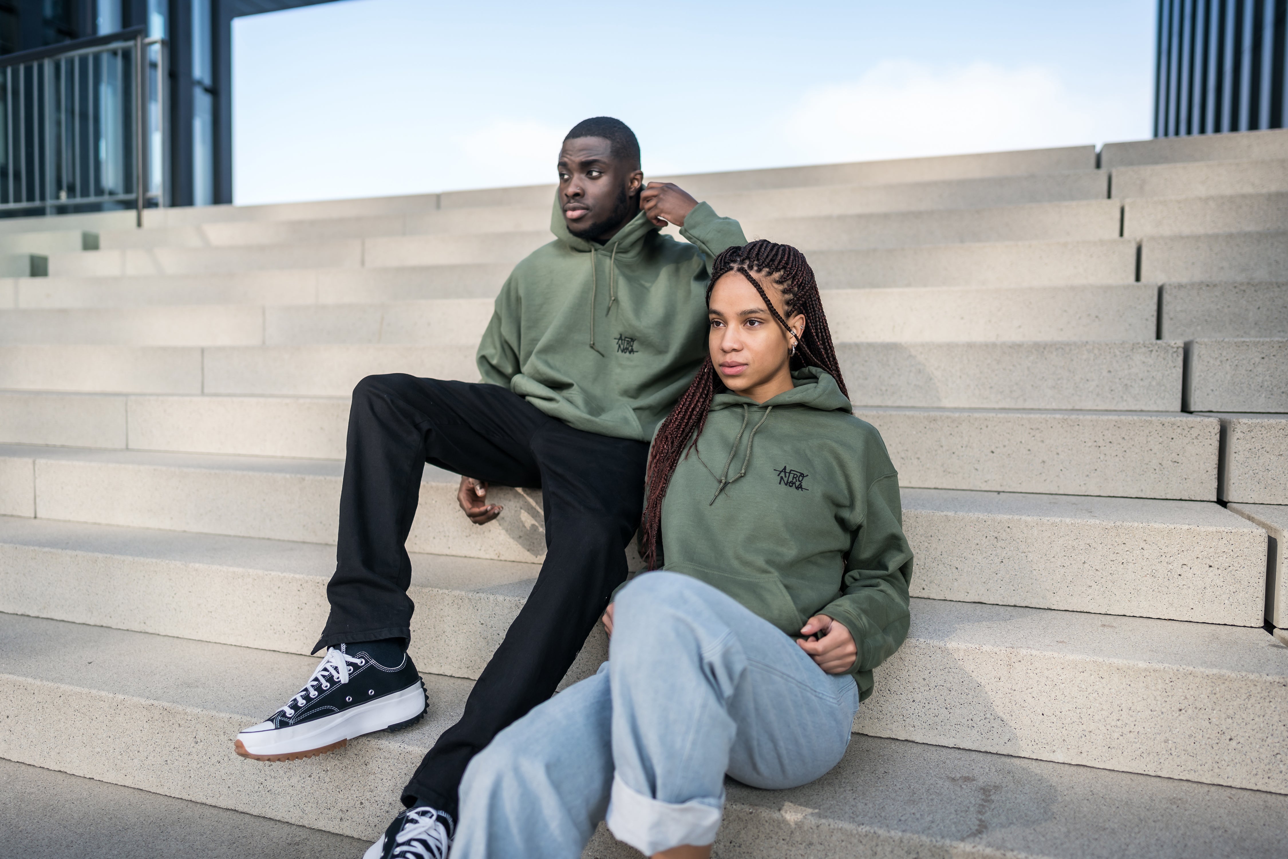 Man and woman sitting on stairs both wearing a military or olive green hoodie